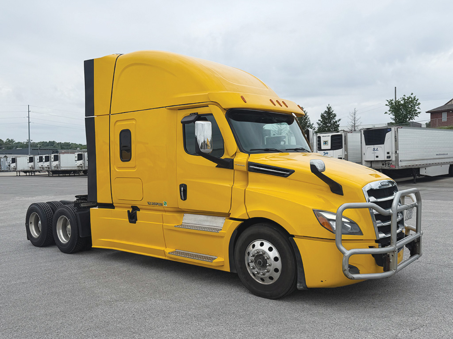 Yellow Freightliner Cascadia126 semi truck in a lot, side view, with sleeper cab and chrome bumper guard.