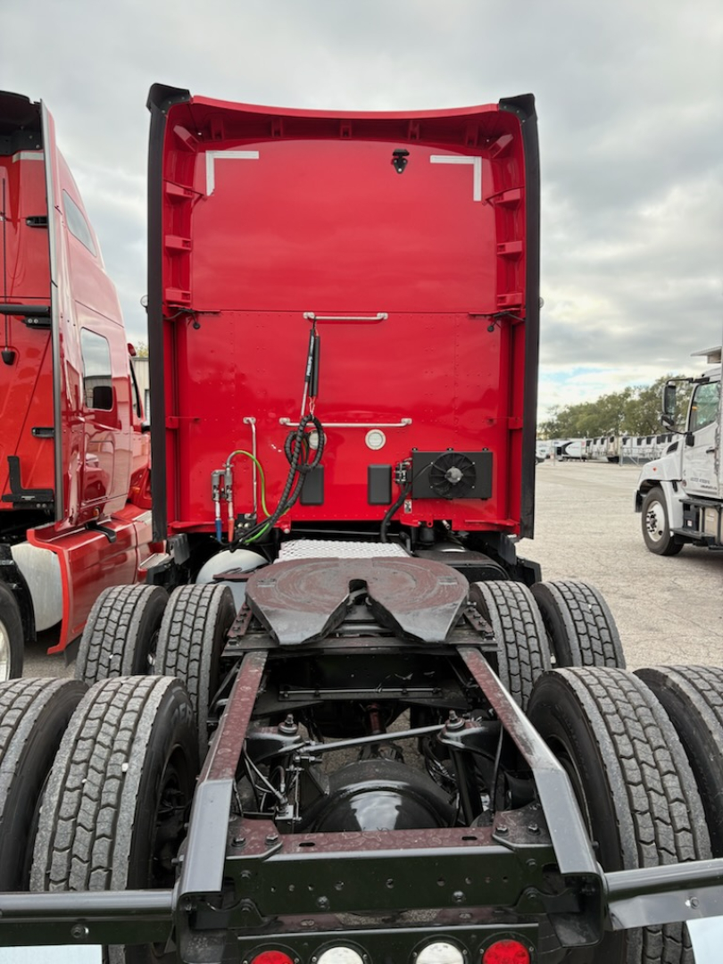 Kenworth T680 chassis and rear cab area showing fifth wheel, drivetrain, and dual rear axles in a truck yard.