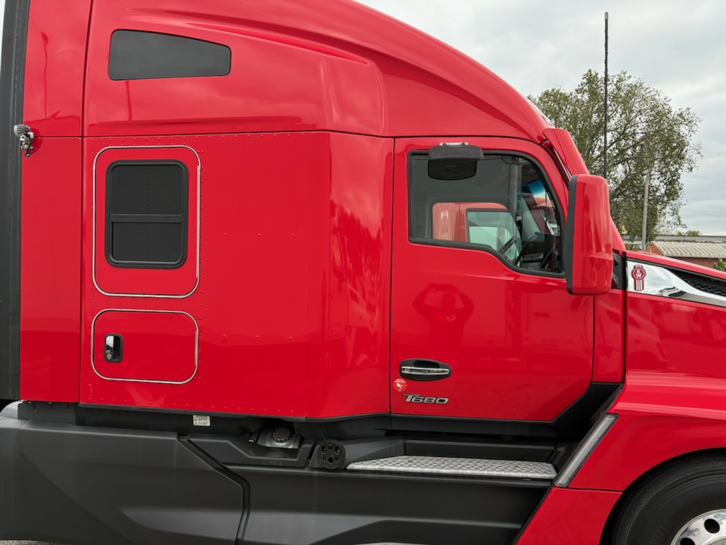 Kenworth T680 sleeper cab side profile in red with black lower trim and side door panels. Visible door outlines and window, cab roof fairing, fuel/step area.