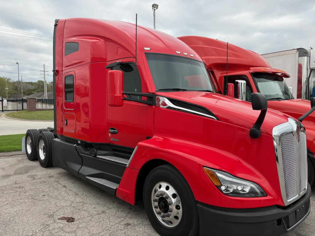 Kenworth T680 sleeper tractor in red, side view showing cab, windshield, front grille, and wheel rims.