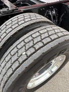 Kenworth T680 front wheel area showing dual rear tires with tread pattern and chrome wheel. Part of the truck chassis and frame visible.