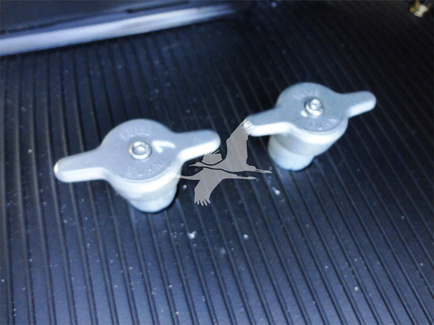 Two silver plastic caps with screws on a ribbed black surface, likely engine bay or toolbox.