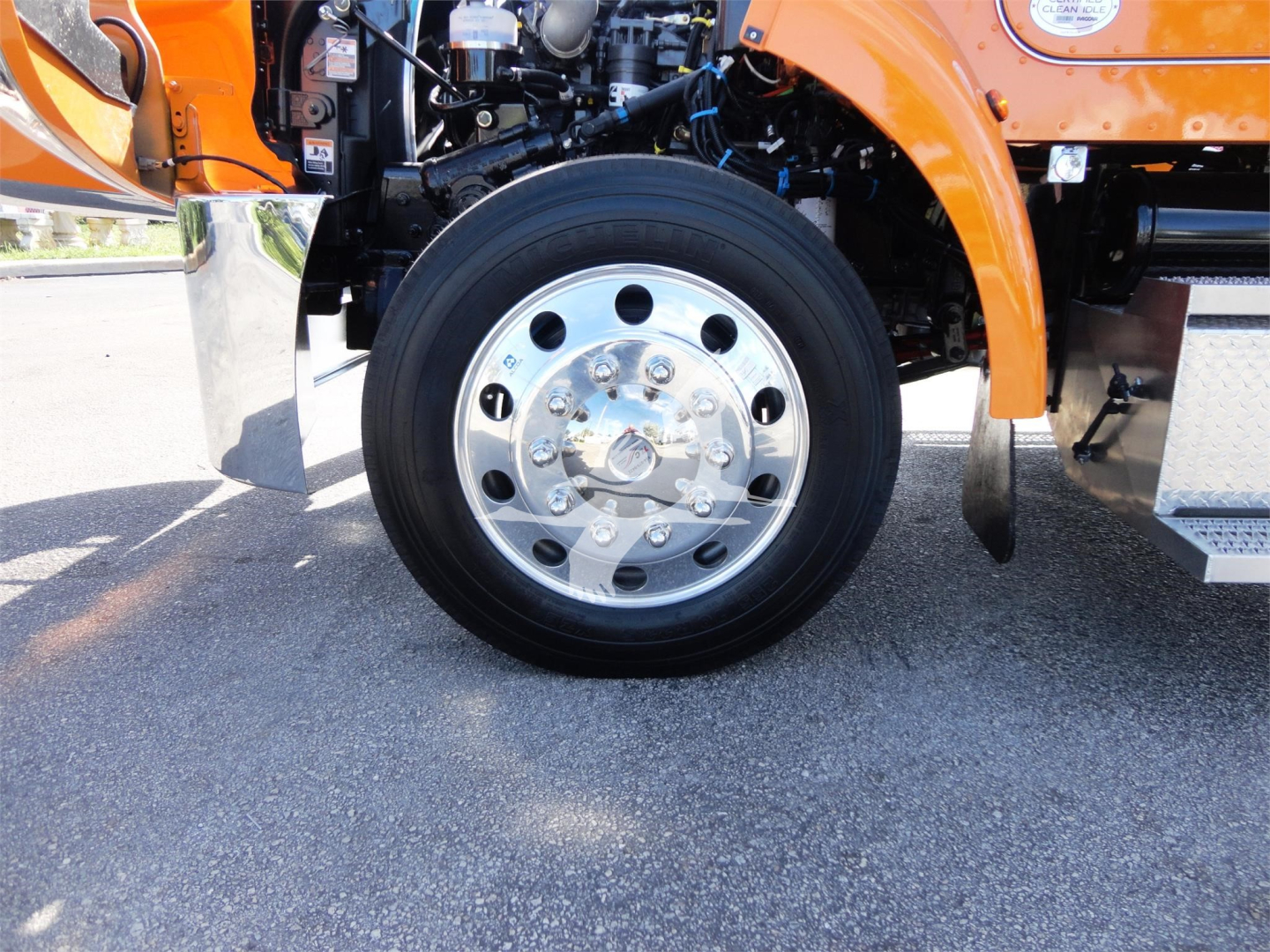Peterbilt 337 front wheel area and chrome wheel with hub showing engine bay components and fender; orange truck body visible.