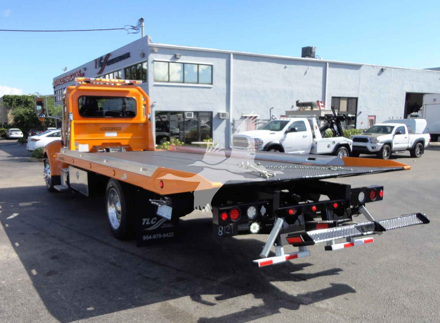 Peterbilt 337 rollback tow truck with flatbed rear, orange cab, black wheels, in a dealership lot.