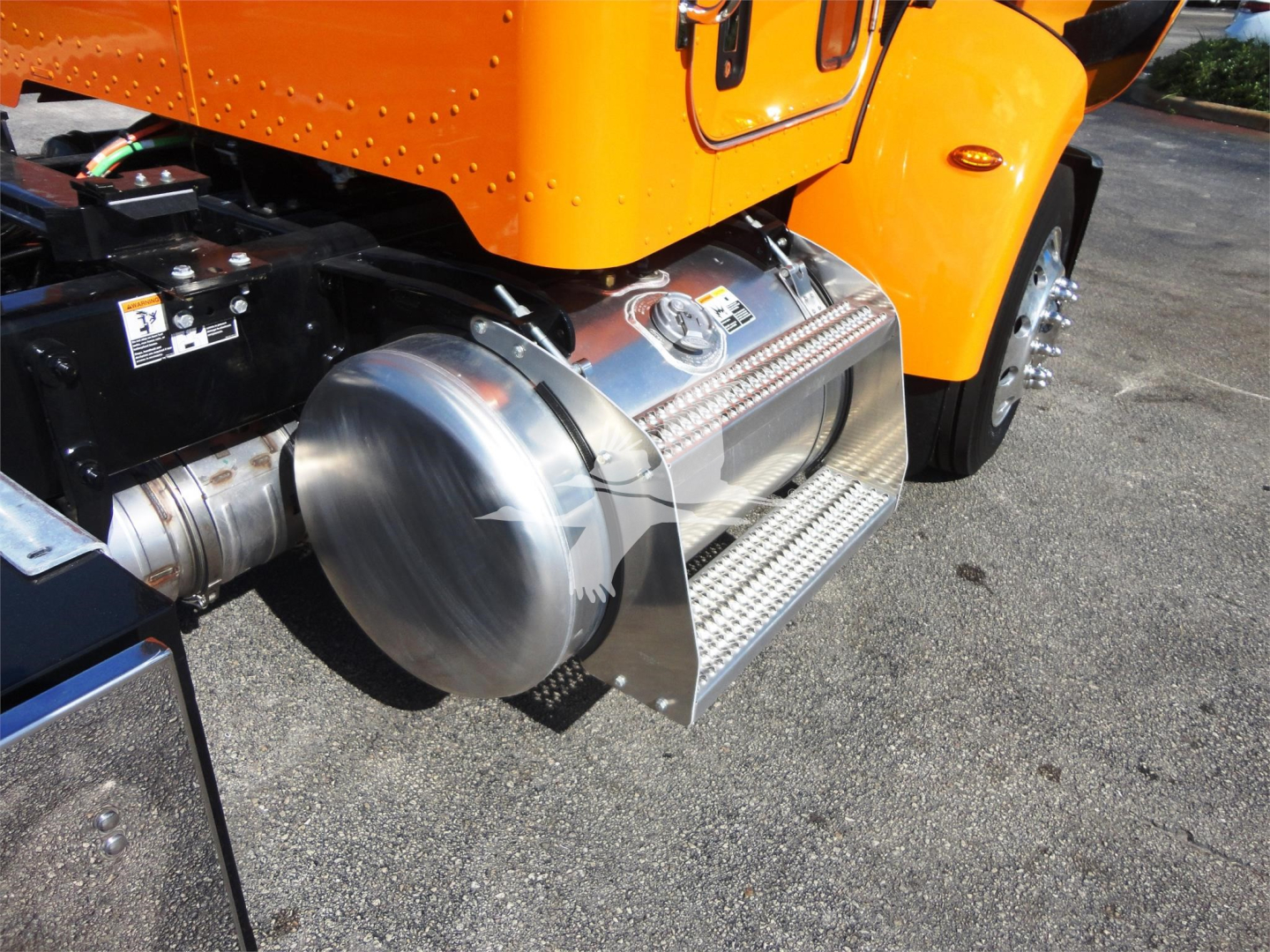Peterbilt 337 side view showing chrome fuel tank guard and side step on orange truck, portion of rear wheel and chassis visible.