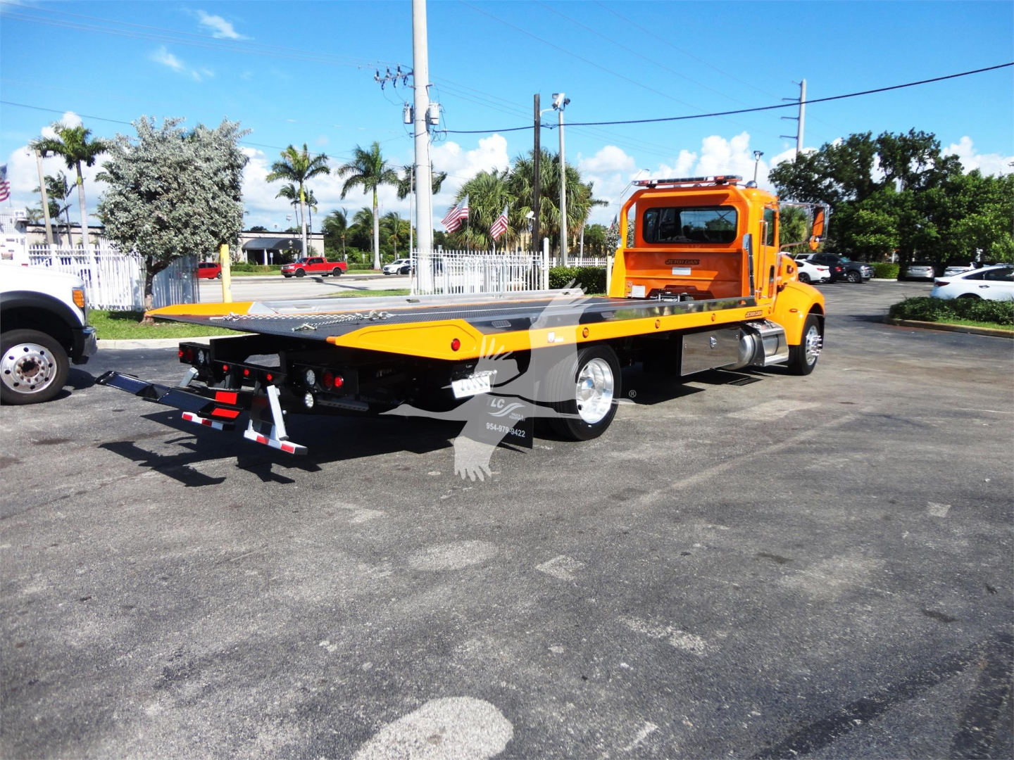 Peterbilt 337 rollback tow truck with orange cab and flatbed viewed from the rear-left side.