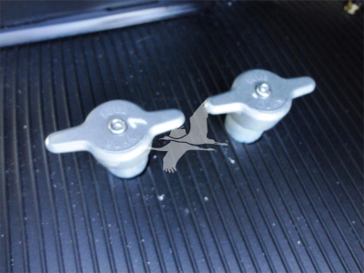 Two silver plastic caps with screws on a ribbed black surface, likely engine bay or toolbox.