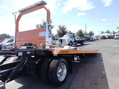Peterbilt 337 rollback wrecker chassis flatbed with orange frame and aerial carrier, dual rear wheels, visible cab area and truck yard in background.