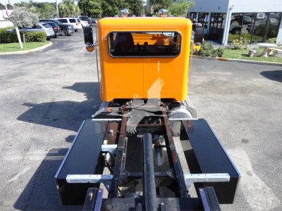 Peterbilt 337 rollback truck chassis with orange cab and black frame rails, front view showing hitch and hydraulic components.