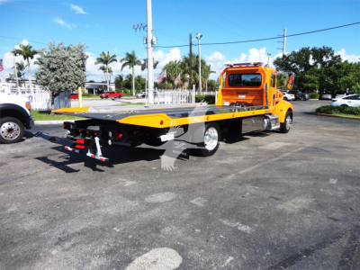 Peterbilt 337 rollback tow truck with orange cab and flatbed viewed from the rear-left side.