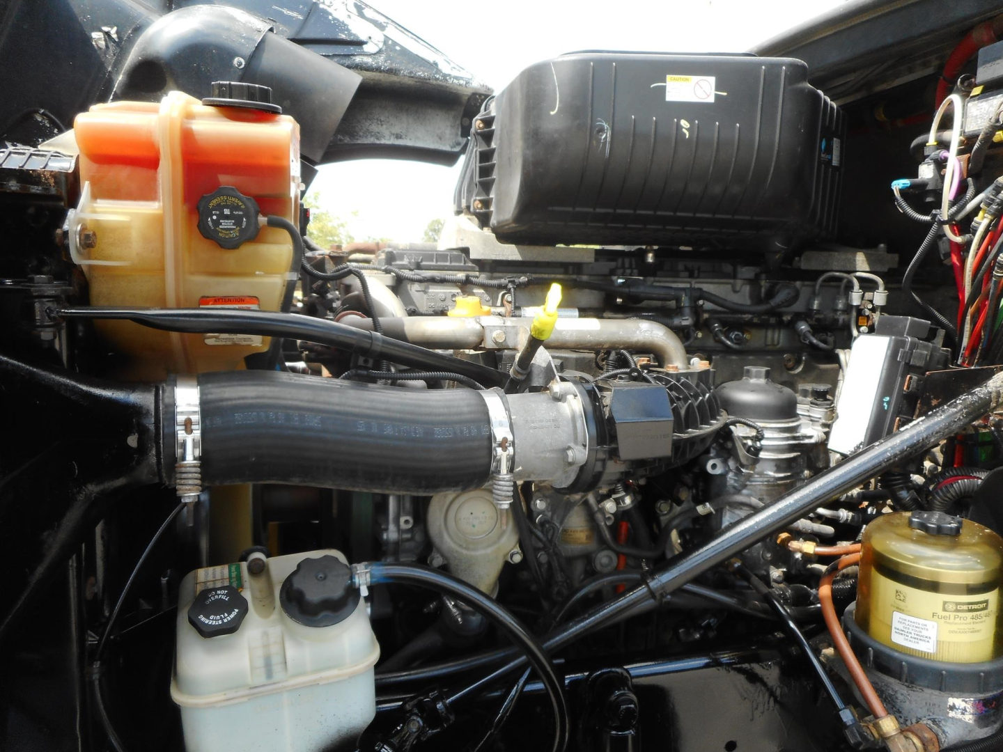 Engine bay of a 2019 Freightliner 122SD showing coolant reservoir, air intake hose, yellow fluid reservoirs, and wiring harnesses.