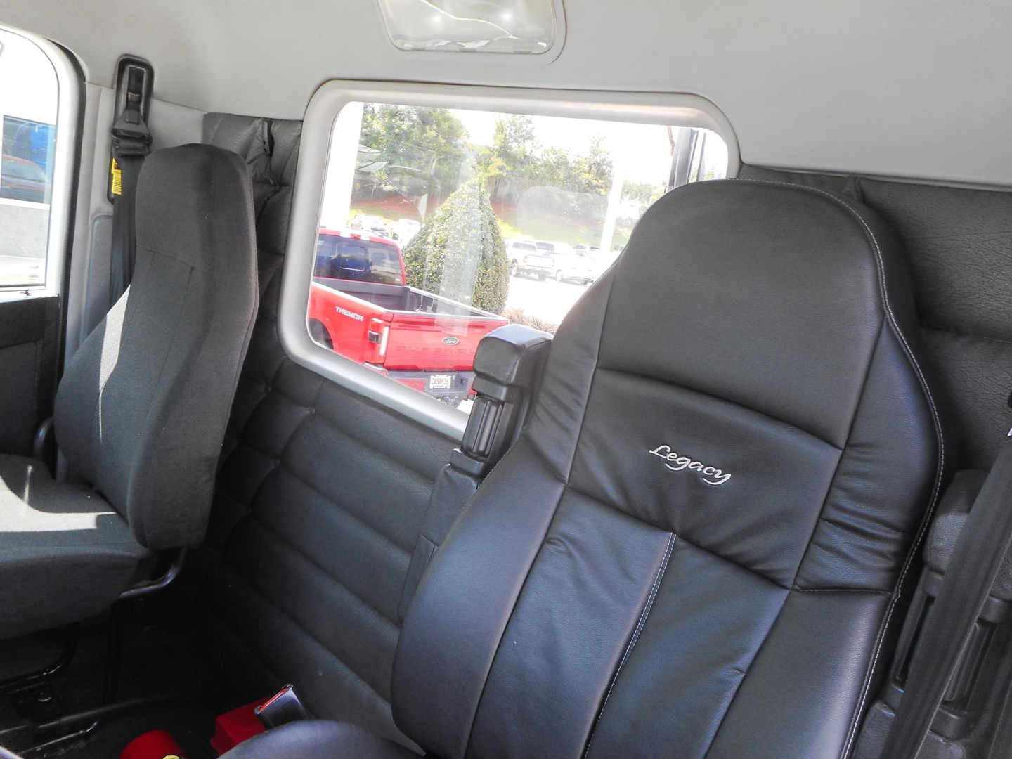 Interior view of a 2019 Freightliner 122SD cab showing perforated black leather seat with 'Legacy' embroidery and window to the side.