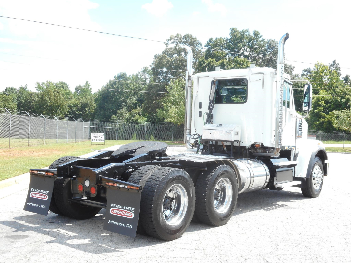 Tractor unit with white cab and chrome exhaust stacks, three rear axles, showing fifth wheel and rear tires; Freightliner 122SD cab with long hood.