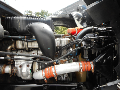 Truck engine bay showing 2019 Freightliner 122SD engine with hoses, turbo intake, and orange silicone hose clamps.