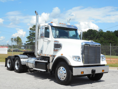 Truck cab and chassis from a Freightliner 122SD with chrome grille, dual exhaust stacks, white cab, three axles, daytime sky.