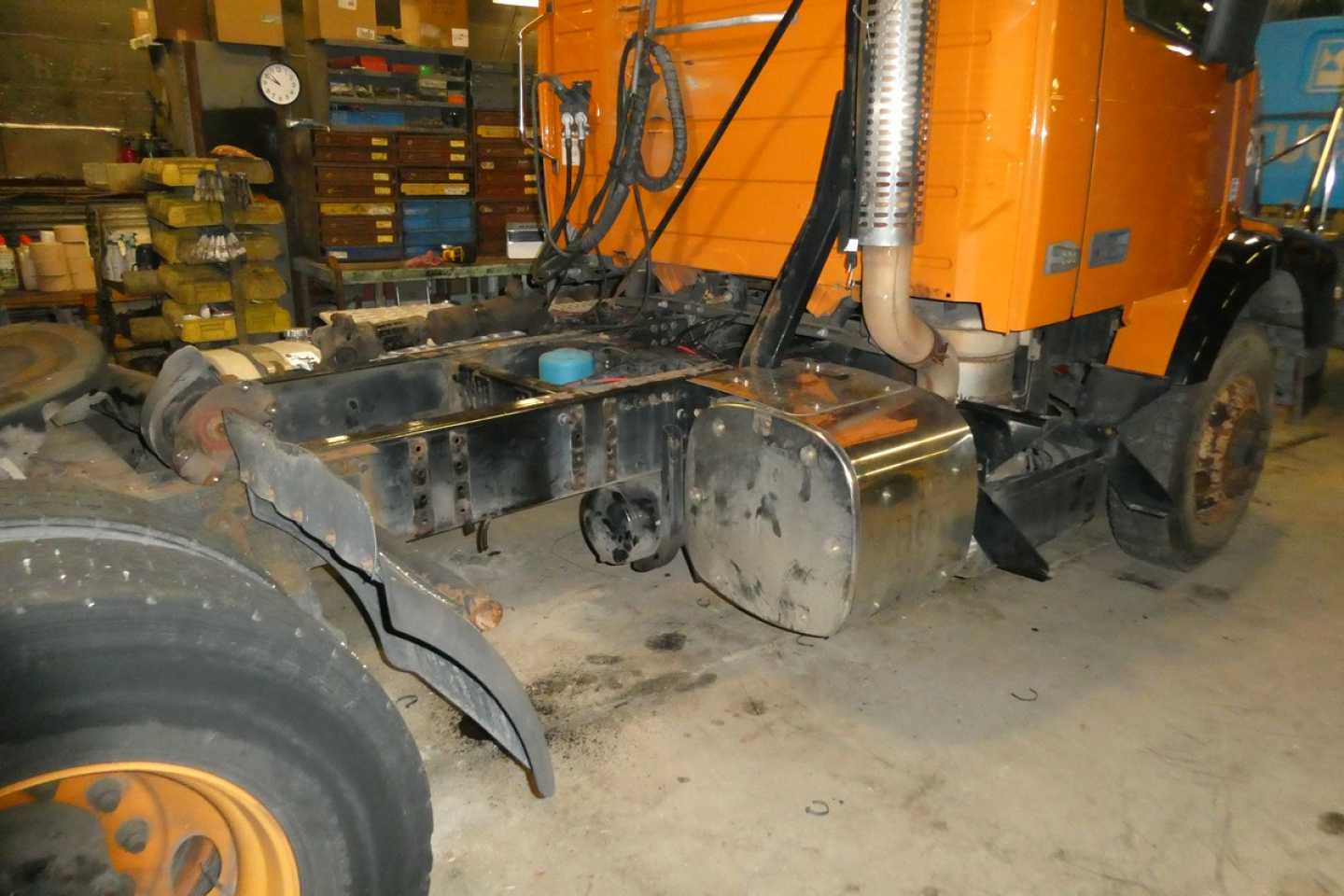 Volvo VNM truck chassis with exposed fuel tank and exhaust, undercarriage view showing frame rails and wheel in workshop.