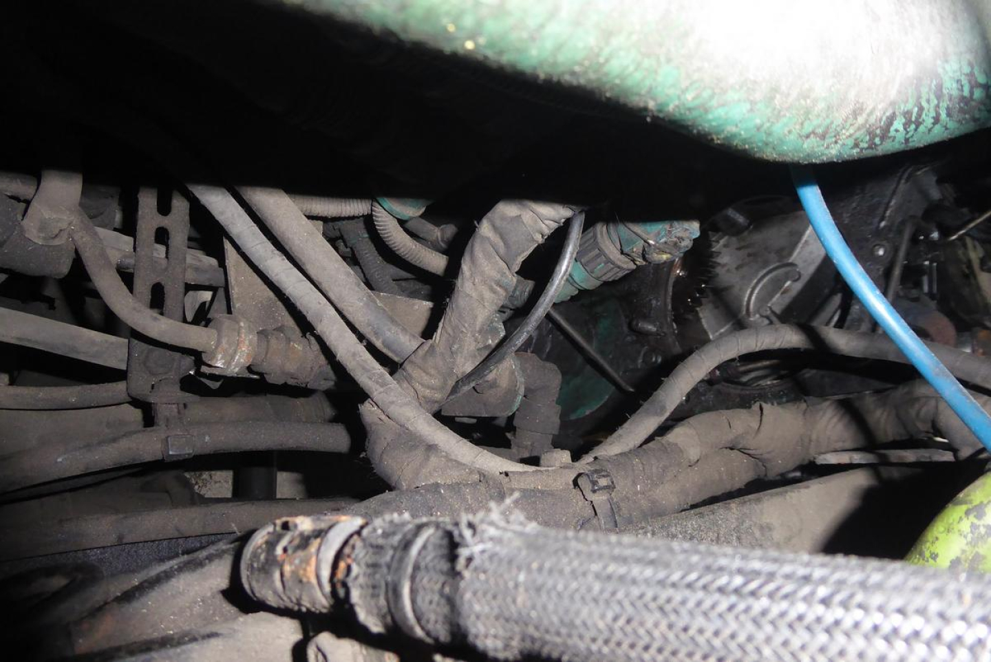 Engine bay view showing tangled hoses and wiring in a Volvo VNM truck, with a blue wire and braided hose visible.