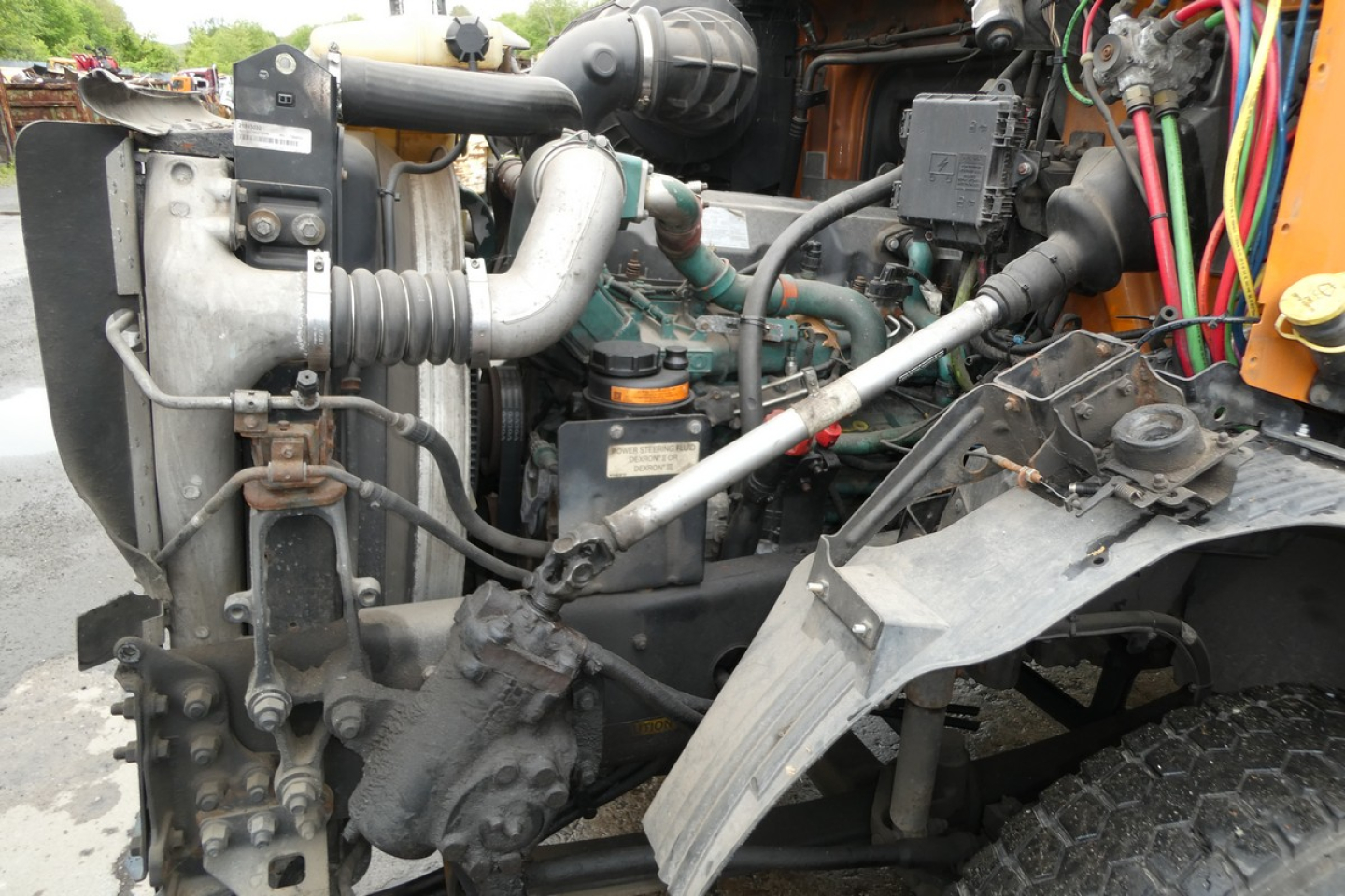 Truck engine bay showing radiator, hoses, turbo, and electrical harnesses; various pipes and components visible; Volvo VNM42T diesel engine area.