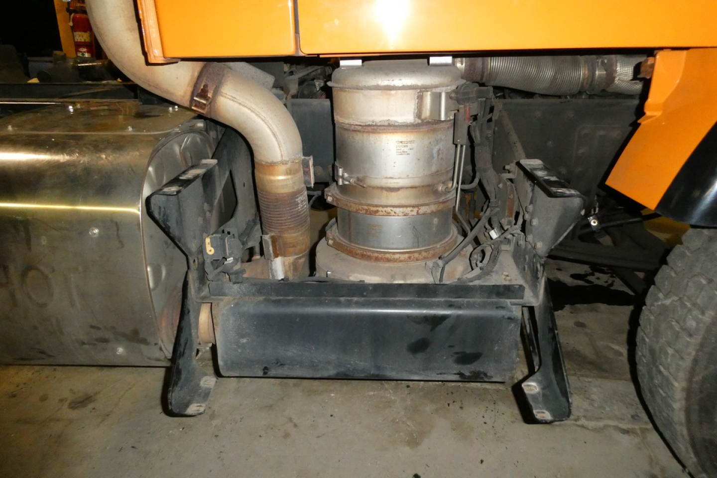 Volvo VNM42T engine bay showing cylindrical exhaust/turbo area and metal skid plate, with hoses and radiator nearby.