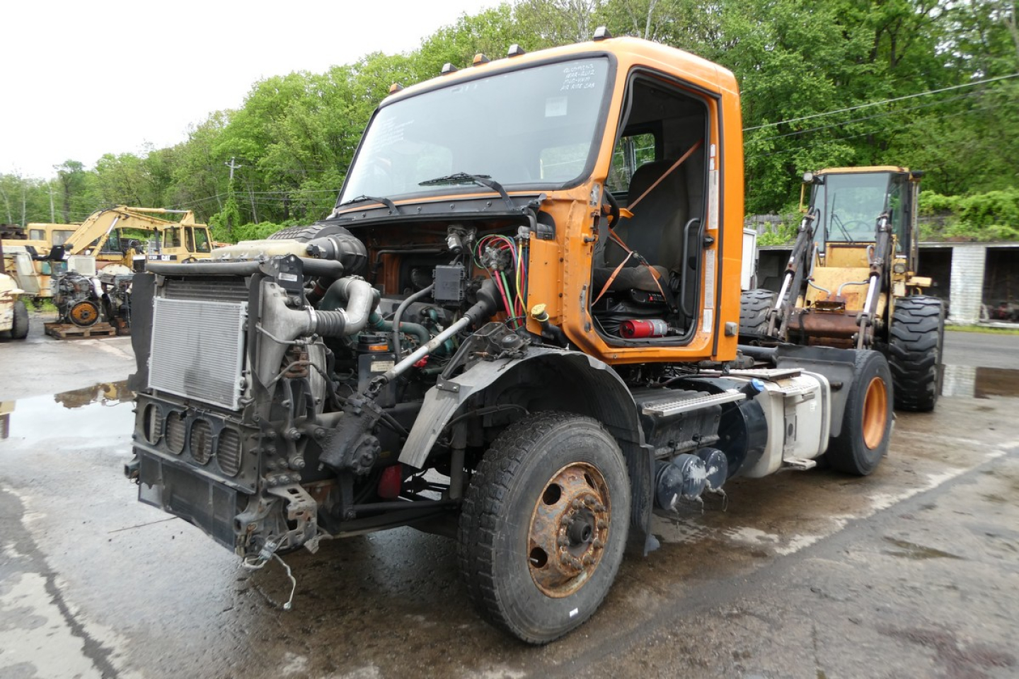 Truck front with engine exposed; orange cab; Volvo VNM42T Daycab, visible radiator, hoses, and damaged front end area.