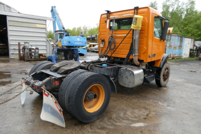 Volvo VNM42T truck tractor rear view showing tandem axle and orange cab with fifth wheel and fuel tank.