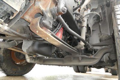 Truck undercarriage view showing suspension and steering components on a Volvo VNM42T. Visible are axle, leaf springs, tie rods, and frame with some rust and grime.