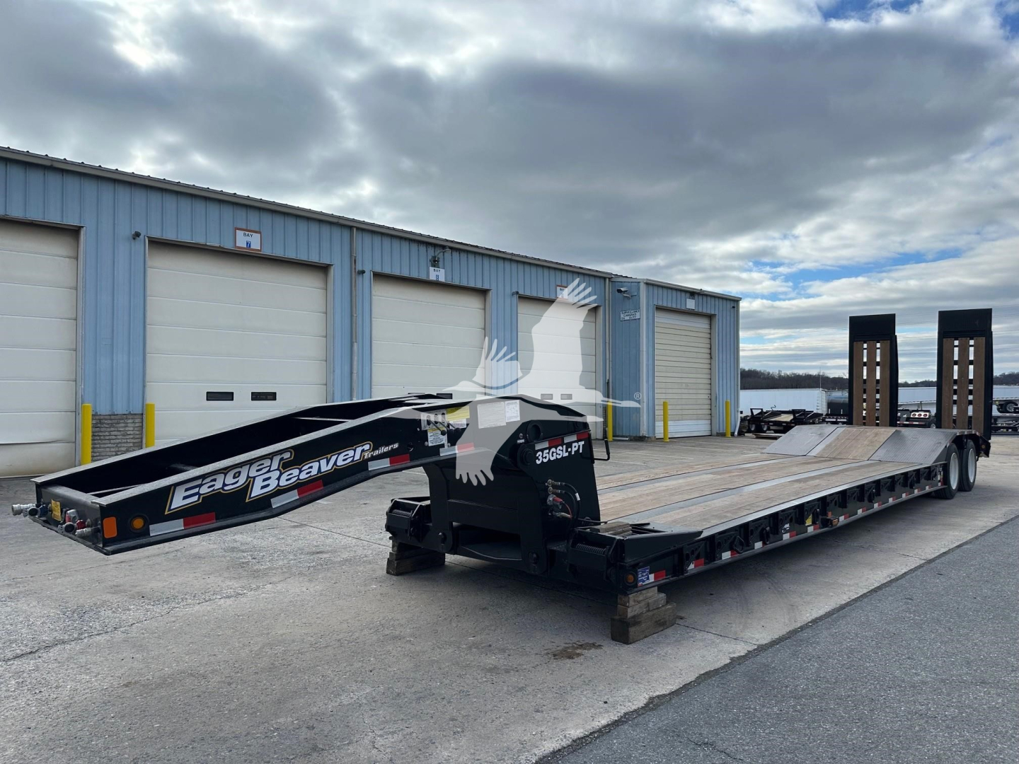Lowboy trailer by Eager Beaver 35Gsl with long flatbed and dual wheel ramps, showing branding and a stylized eagle graphic on the side.
