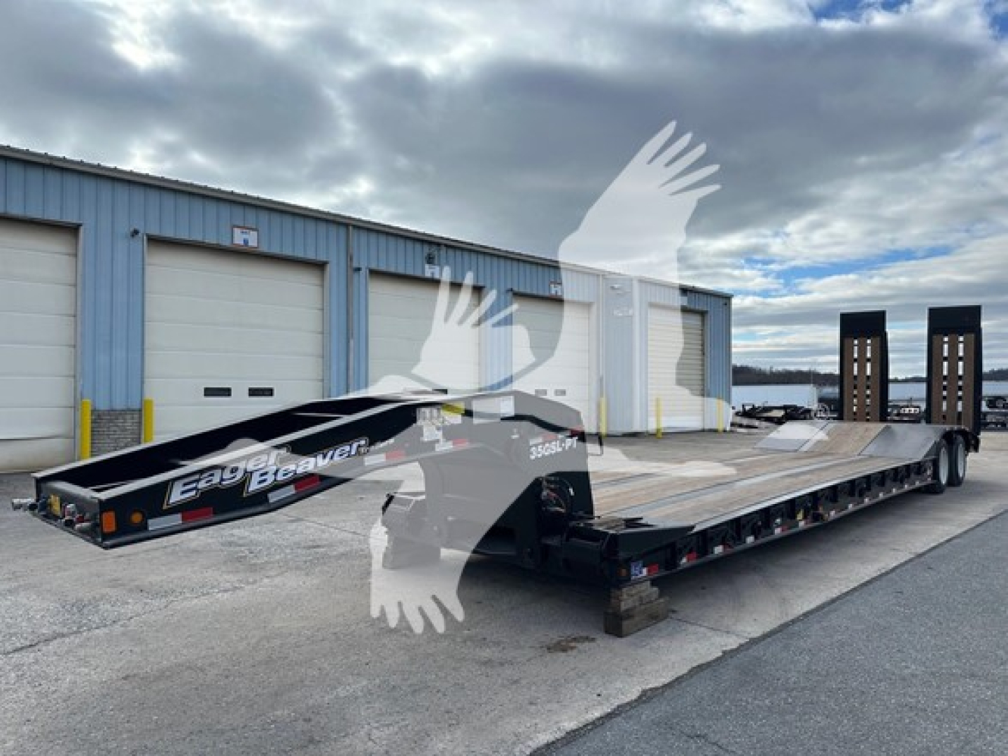 Lowboy trailer with ramp to load equipment, showing flatbed deck and dual axles, Eager Beaver branding on side, set in a storage yard.