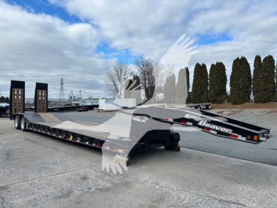 Lowboy trailer with long flatbed and gooseneck, Eager Beaver branding on side, ramps folded, trailer in yard.