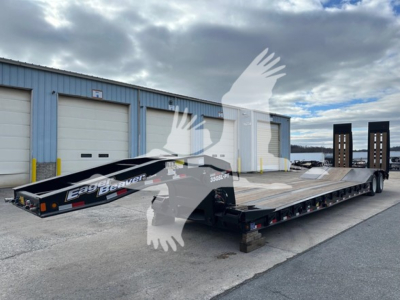 Lowboy trailer with ramp to load equipment, showing flatbed deck and dual axles, Eager Beaver branding on side, set in a storage yard.