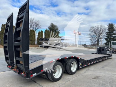 Trailer deck of a lowboy trailer showing dual axles and loading ramps raised at rear with black frame and white wheels.