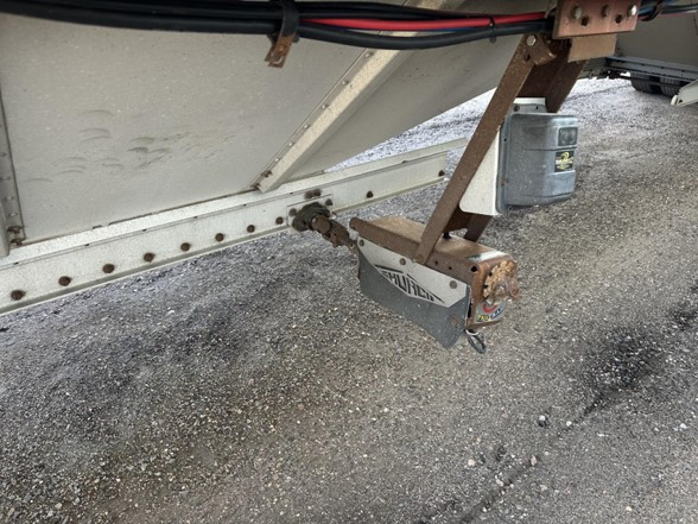 Hopper trailer hitch and coupler area showing a Merritt trailer hitch with safety chains and jack under a trailer frame.