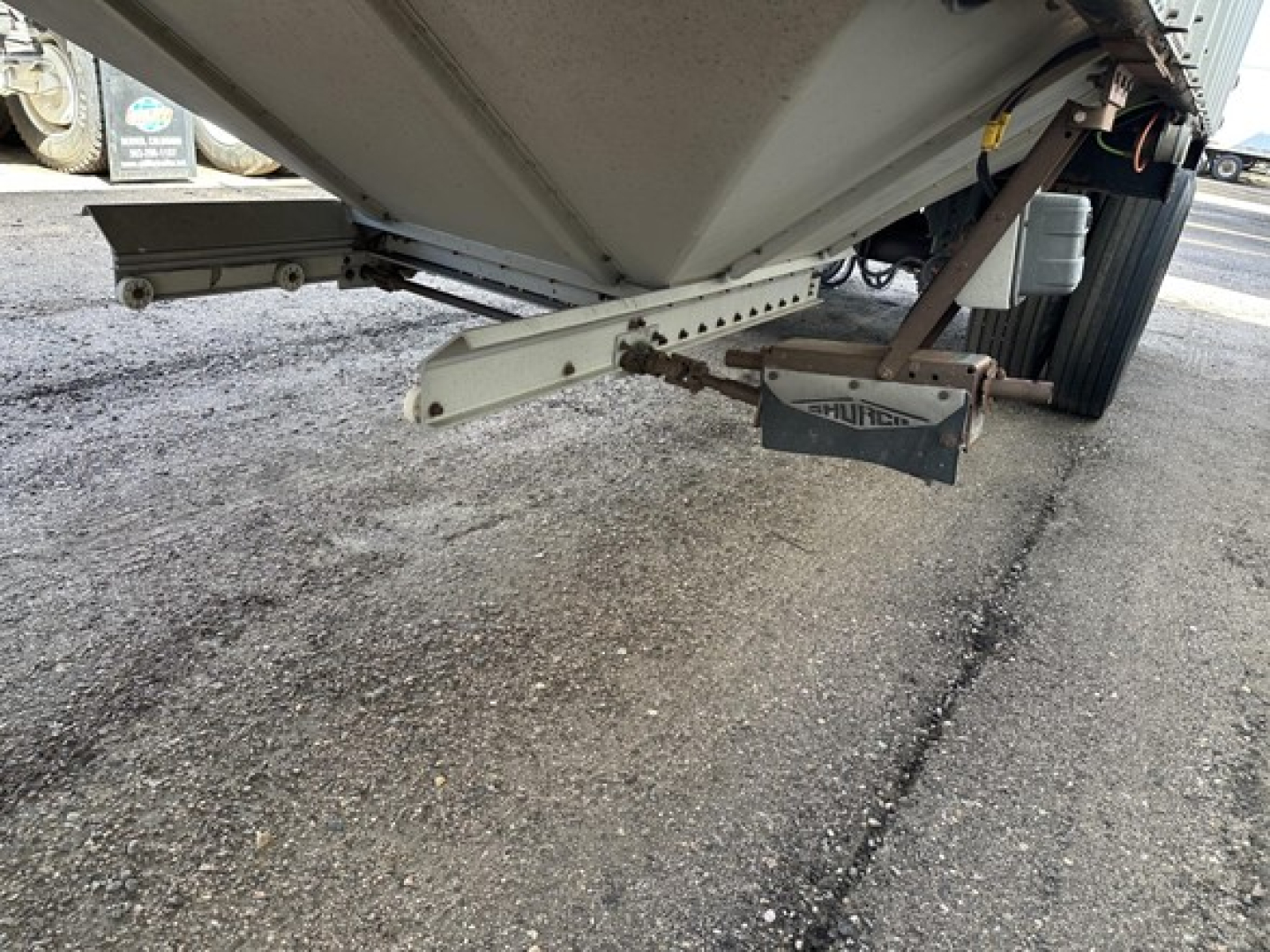 Hopper trailer underside with loading chute and aerodynamic pin, 2015 Merritt Heritage model, showing suspension arm and identification plate.