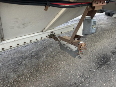 Hopper trailer hitch and coupler area showing a Merritt trailer hitch with safety chains and jack under a trailer frame.