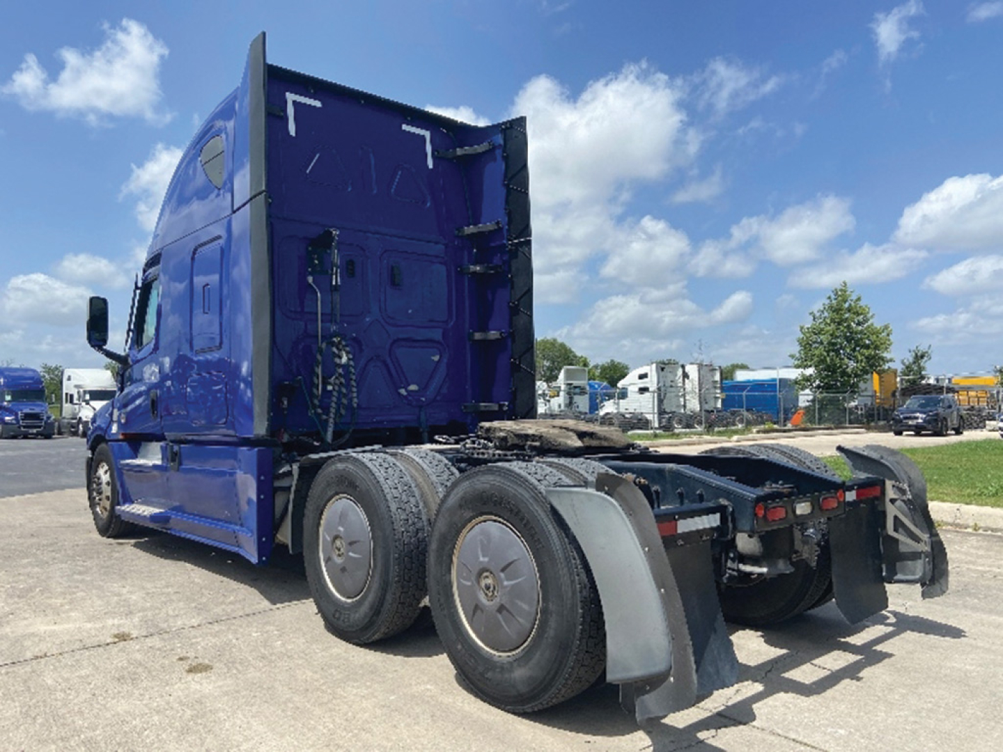 Truck cab from rear-left view of a blue 2022 Freightliner Cascadia126 with extendable sleeper, chassis, dual rear axles, and fenders visible.