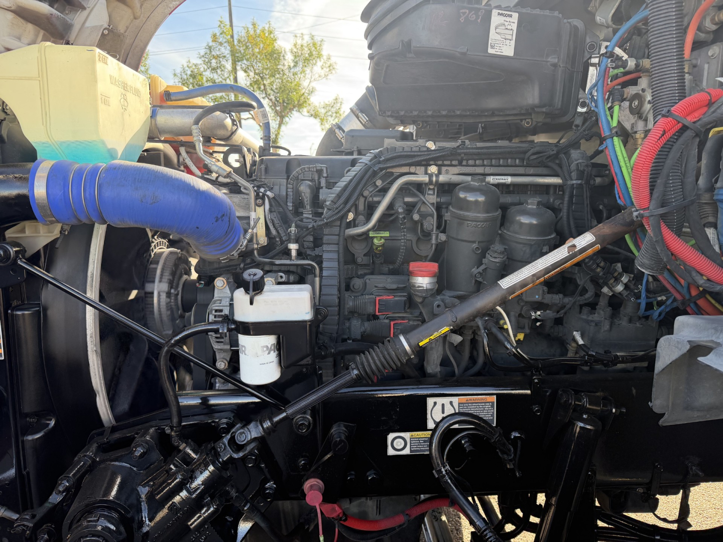 Kenworth T880 engine bay with multiple hoses, hoses, and wiring harnesses visible; engine components, coolant reservoir, and air intake visible.