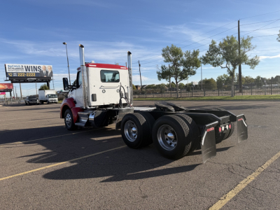 Kenworth T880 conventional daycab tractor rear view showing dual rear axles and fifth-wheel, with white and red cab and black chassis.