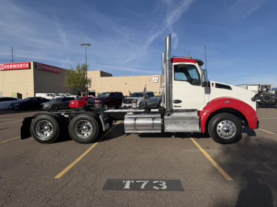 Kenworth T880 conventional daycab side view showing chassis and rear axles, with white cab and red accents in parking lot.