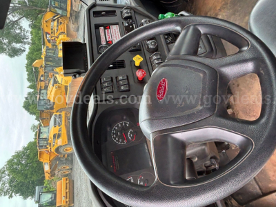 Peterbilt truck cockpit view showing steering wheel and dashboard with gauges; yellow heavy equipment vehicles visible through window.