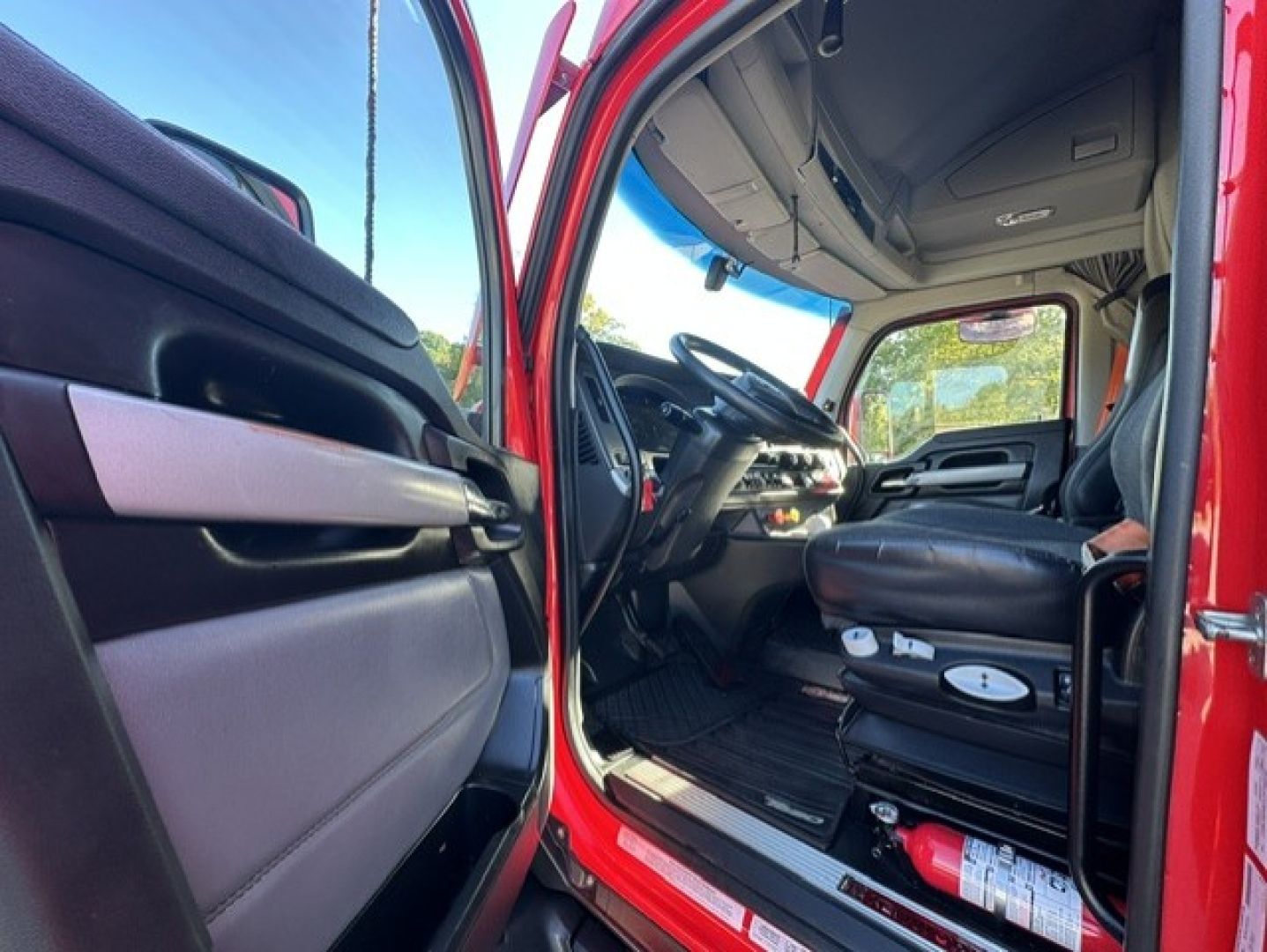 Kenworth T680 truck cab interior showing driver's seat and dashboard with steering wheel and open door.