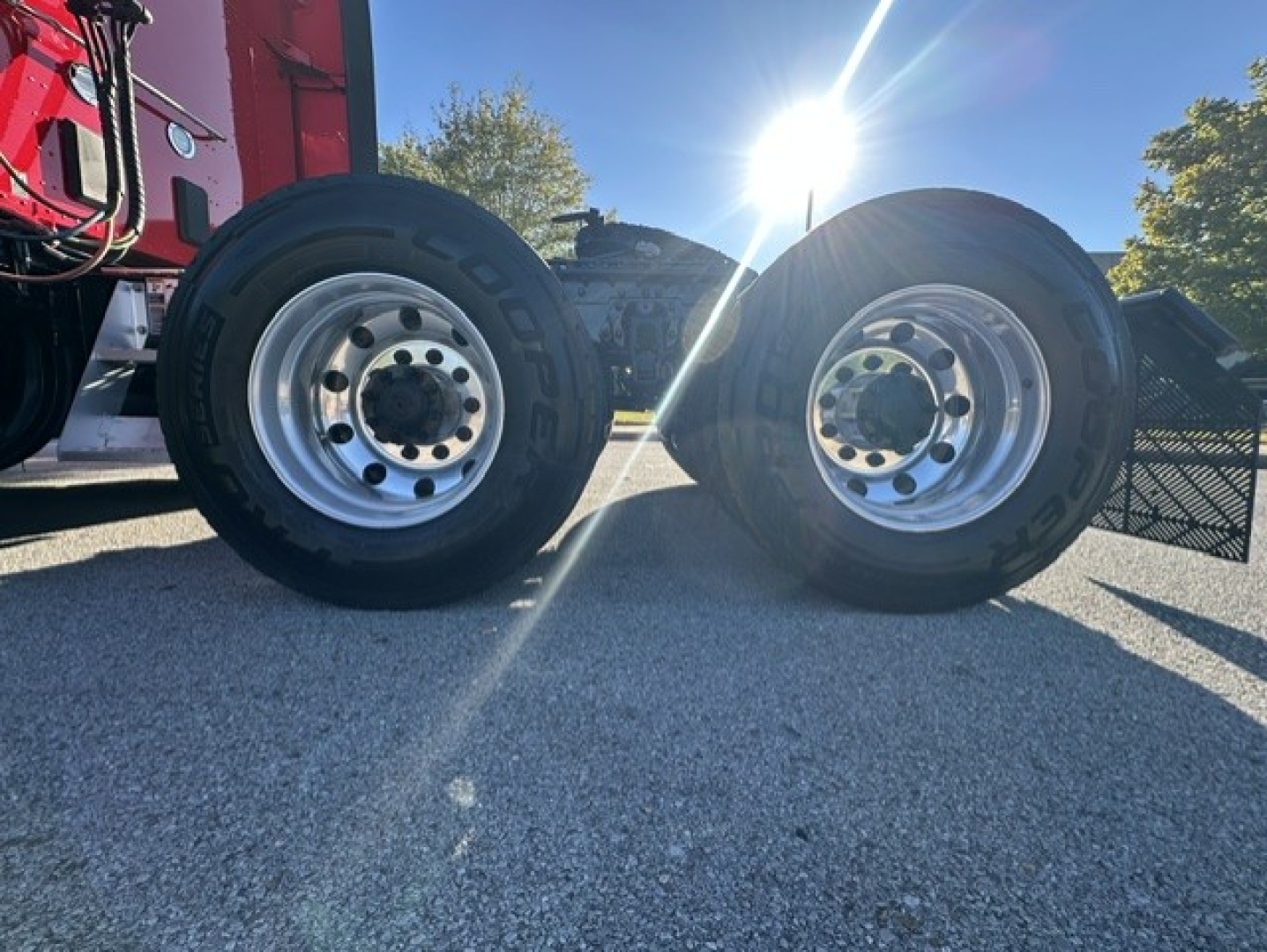 Kenworth T680 wheel set with dual rear axles and polished steel rims, daylight highlighting the tires.