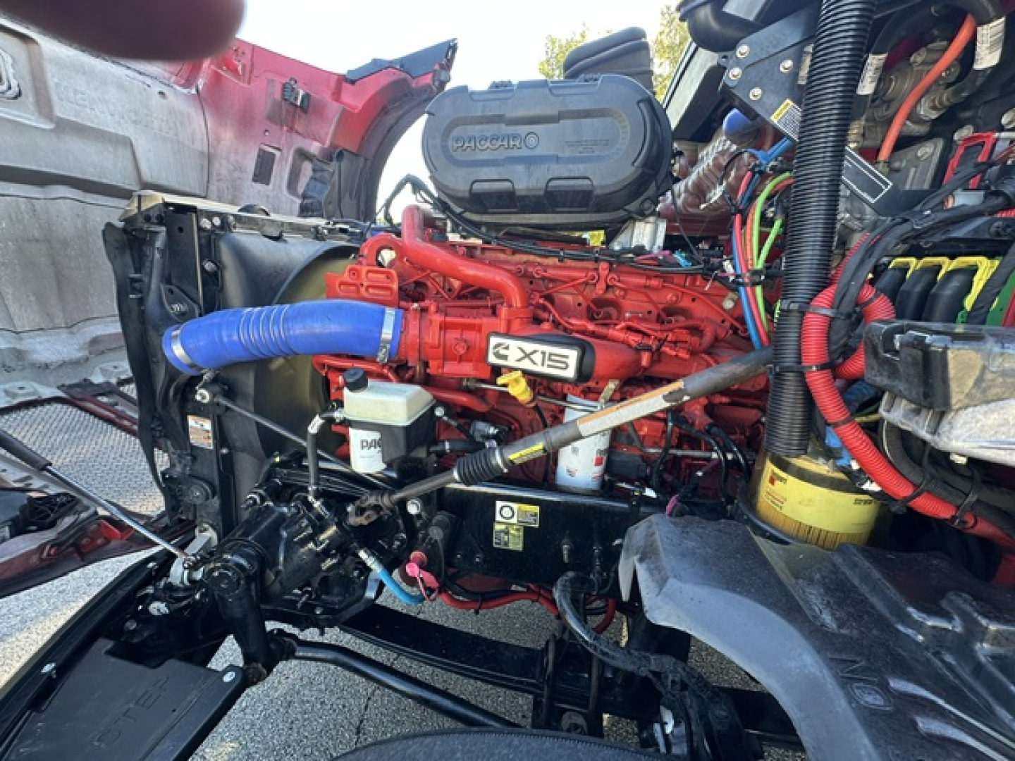 Kenworth T680 engine bay with red Ex6 labeled engine, blue turbo hose, and various wiring; shows diesel engine components and surrounding chassis.
