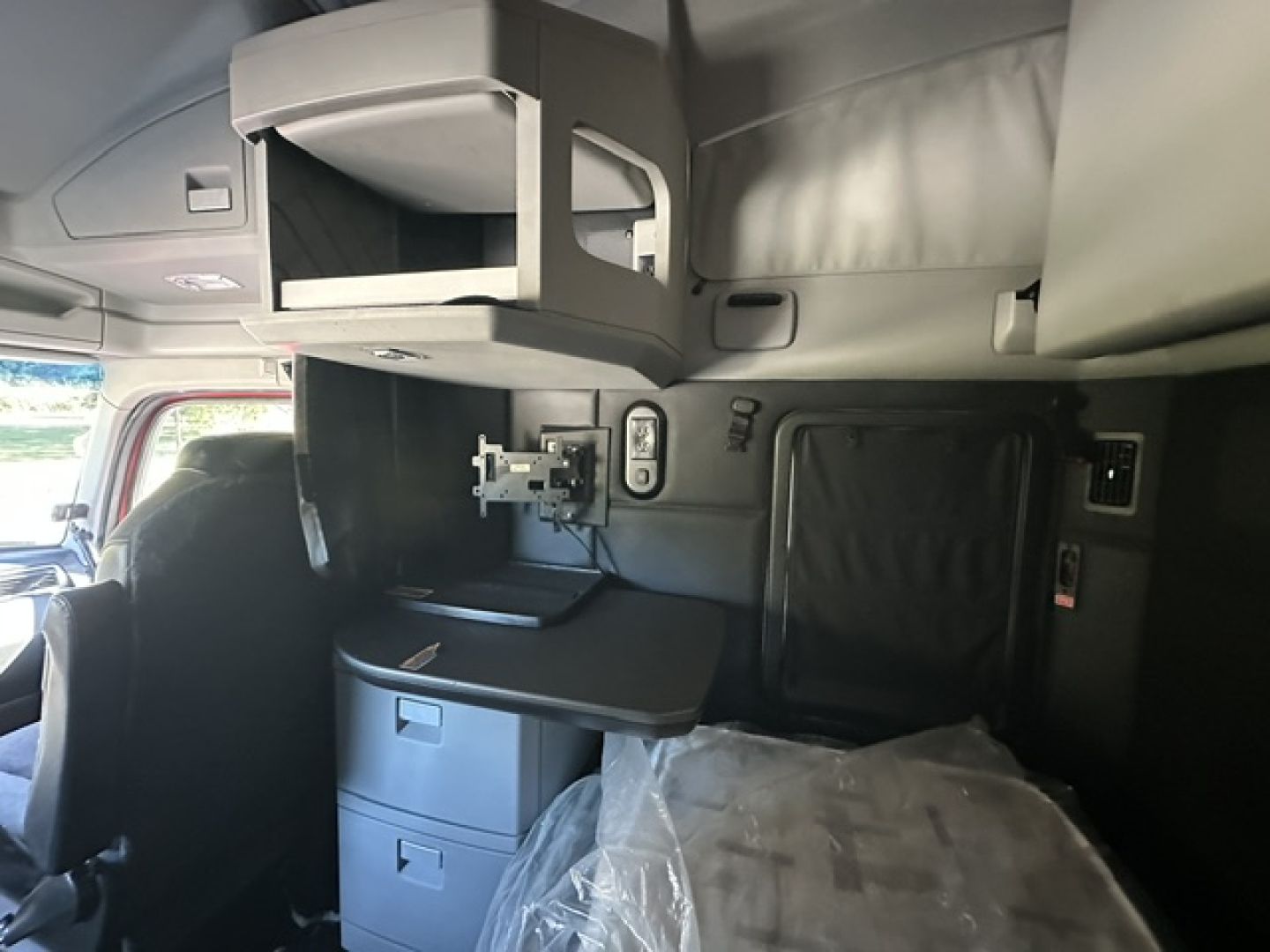 Kenworth T680 sleeper cab interior showing overhead storage shelf and mounted TV/monitor bracket with desk area and side panel controls.