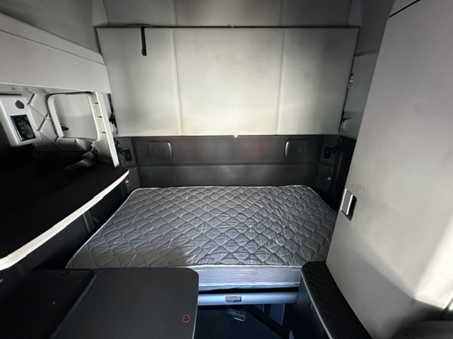 Kenworth T680 sleeper cab interior with folded bunk bed in view, quilted mattress, and side paneling.