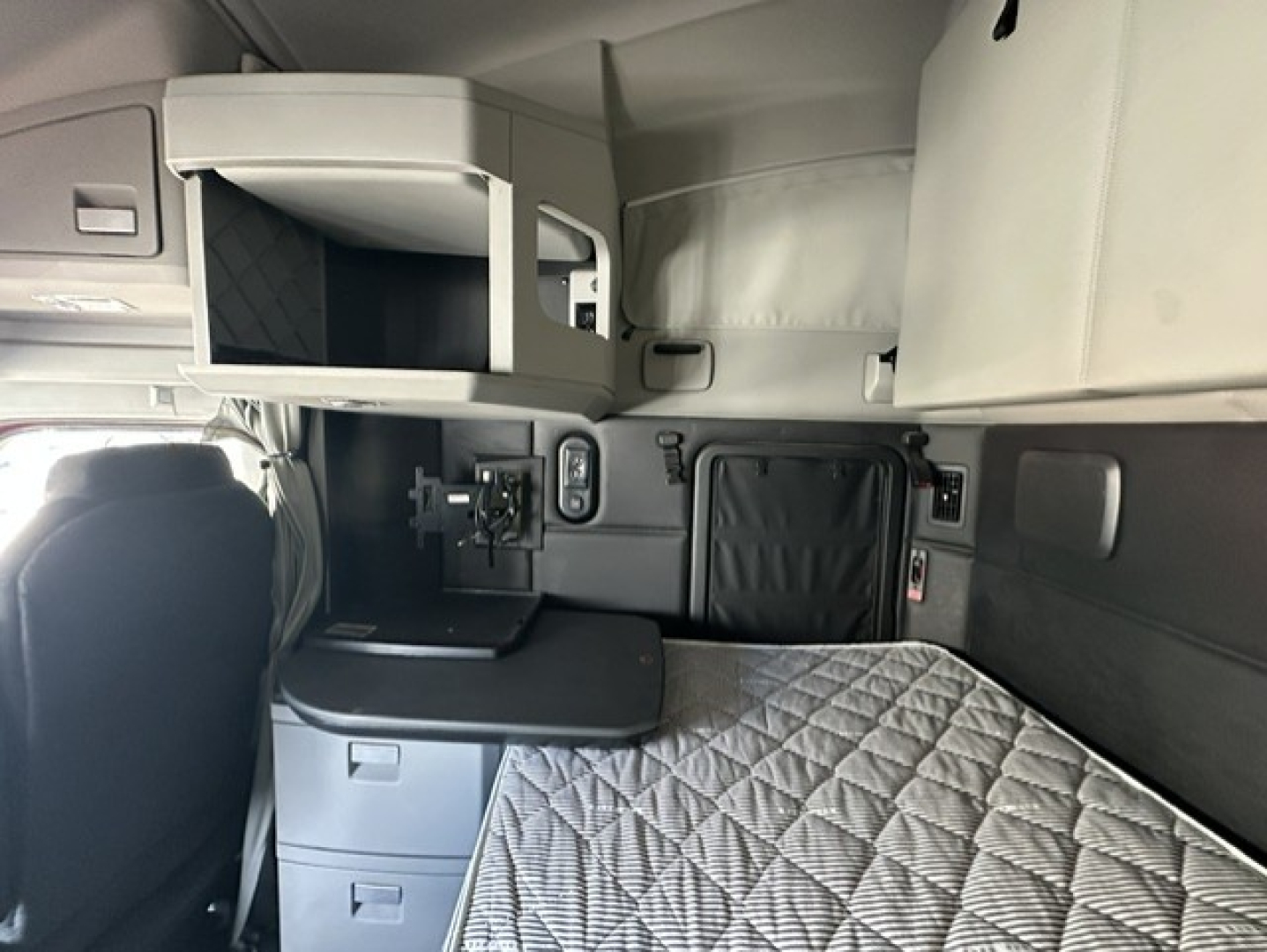 Cabin area of a 2023 Kenworth T680 sleeper, showing bunk bed with quilted mattress, side storage drawers, and upper compartment in view.