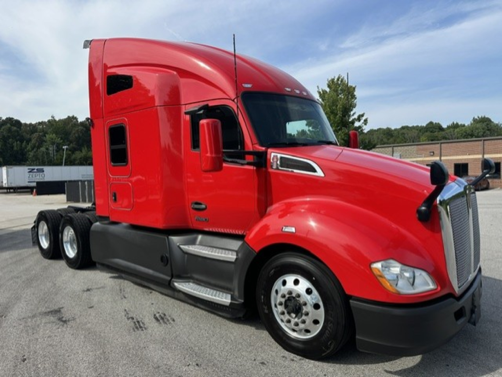 Kenworth T680 sleeper cab truck in red with three axles, front view showing cab with aerodynamic mirrors and chrome steps.