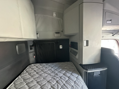 Kenworth T680 cab interior view with sleeping bunk and overhead storage, showing light gray upholstery and compact console area.
