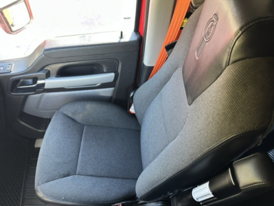 Kenworth T680 truck interior seat and door panel view, cloth seat with Kenworth logo on headrest; driver-side cabin area visible with window, door handle, and armrest.