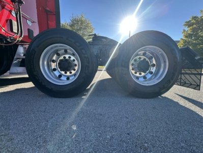 Kenworth T680 wheel set with dual rear axles and polished steel rims, daylight highlighting the tires.