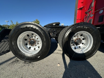 Kenworth T680 tractor rear quad wheel view showing dual drive tires and wheel rims with suspension components; part of truck chassis visible.